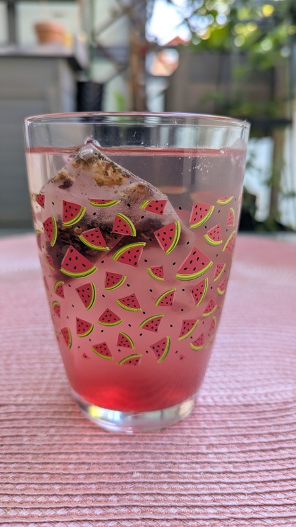 Glas mit Wassermelonenmuster, in dem Eiswürfel im Eistee schwimmen. Das Glas steht auf einem rosafarbenen Platzset.