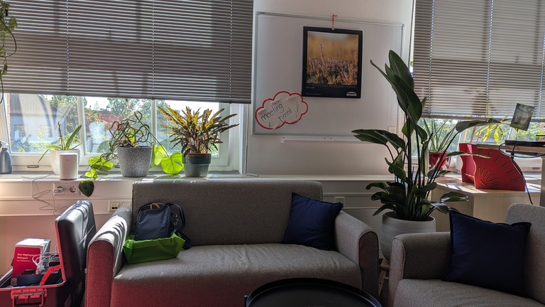 Zwei gemütliche Sofas stehen L-förmig in einem Raum. Im Hintergrund hängt ein Schild, der die Sitzecke als „meeting point“ ausweist.