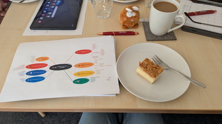Ein Stück Bienenstich auf einem weißen Teller. Daneben steht eine Tasse Kaffee auf dem Tisch.