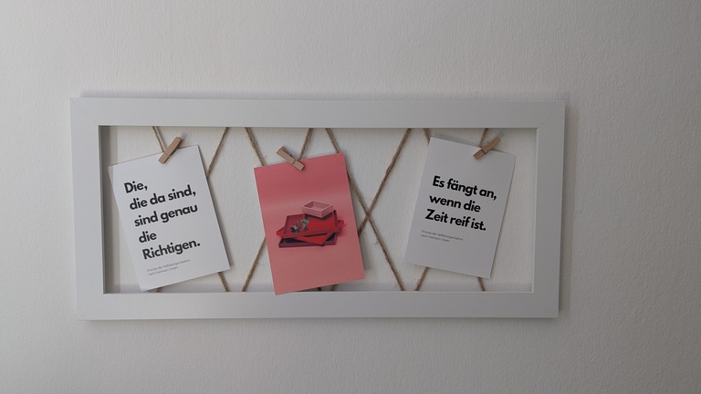 Zwei Sinnsprüche in einem Bilderrahmen, aufgehängt an kleinen Klammern.