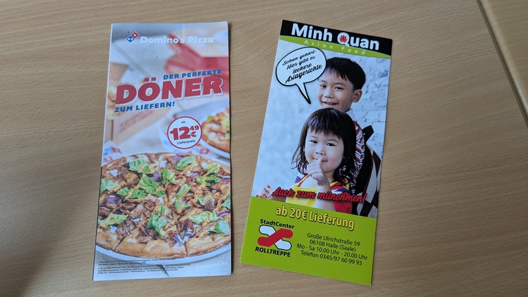 Je ein Flyer der Essenslieferdienste Domino’s Pizza und Minh Quan liegen auf einem Tisch.